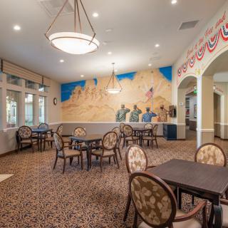 A spacious dining room with multiple tables and chairs, featuring a colorful mural on the wall and elegant lighting fixtures.