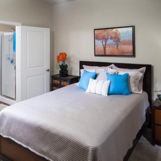 A modern bedroom with stylish decor, featuring a neatly made bed with blue and white pillows and a landscape painting above the headboard.