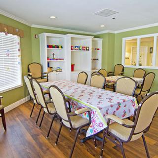 A spacious dining room featuring a long table surrounded by chairs, with green walls and ample natural light.