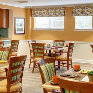 A cozy dining room with neatly arranged tables and chairs, featuring warm decor and natural light from the windows.