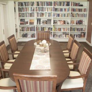 A cozy library room with a long table surrounded by chairs and filled with bookshelves.