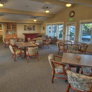 A cozy dining room with multiple tables and chairs set up, featuring large windows for natural light.