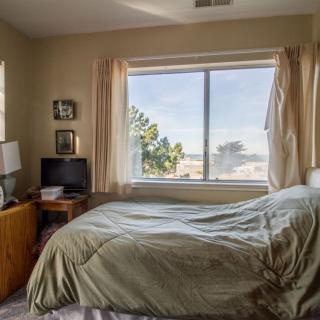 A cozy bedroom with a bed, television, and a large window letting in natural light.