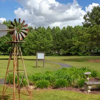 A scenic view of a garden with a windmill and lush green surroundings under a partly cloudy sky.