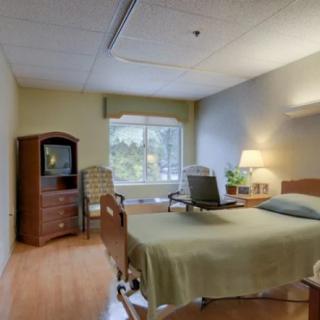 A well-lit hospital room with a single patient bed, television, and a window view.