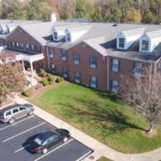 Aerial view of a brick building with a parking lot in the foreground and trees around.