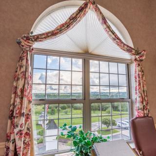 A bright room with a large arched window adorned with floral curtains, offering a scenic view of the outdoors.