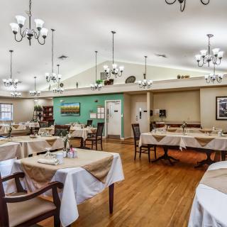 A spacious dining area with neatly arranged tables and chairs, elegant chandeliers, and a warm wooden floor.