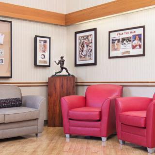 A cozy waiting room featuring a grey sofa, red armchairs, and framed artwork on the walls.