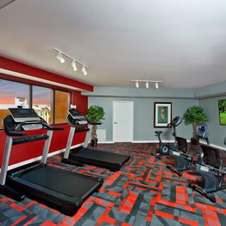 A modern gym area featuring treadmills, elliptical machines, and a vibrant red and grey color scheme.