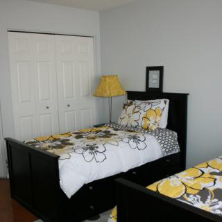 A cozy bedroom with twin beds featuring floral bedding, a lamp, and a closet in the background.