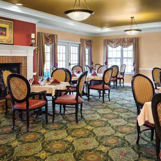 An elegant dining room with neatly arranged tables and chairs, featuring large windows with curtains and a decorative carpet.