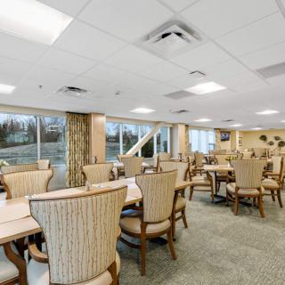 A spacious dining room with several tables and chairs, well-lit by large windows.