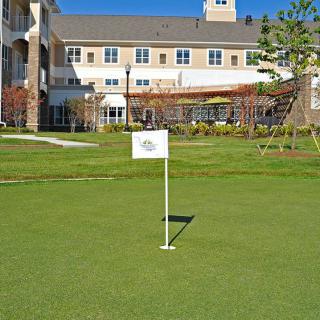A putting green located in front of a large building, featuring a small flag on the course.