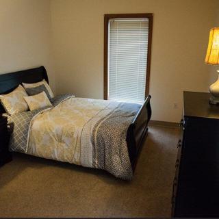 A cozy bedroom with a neatly made bed, bedside lamp, and a window with blinds.