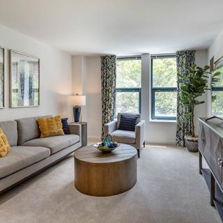 A cozy living room with a modern design, featuring a comfortable sofa, coffee table, and large windows with patterned curtains.