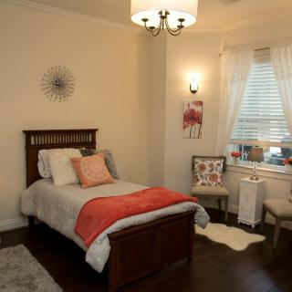 A cozy and well-decorated bedroom featuring a single bed with red accents, a chandelier, and a neatly arranged window area.