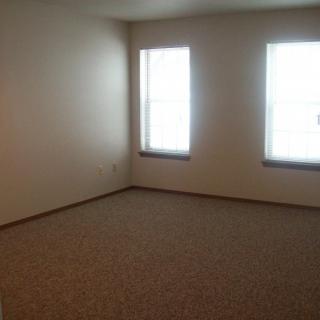 An empty room with carpet flooring and two windows.