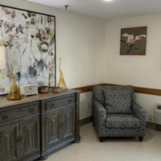 A cozy corner of a room featuring a patterned armchair, a wooden cabinet adorned with decorative items and lamps, and abstract artwork on the walls.