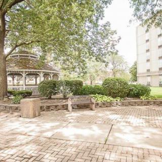 A peaceful park scene featuring a gazebo, benches, and lush greenery under the sunlight.