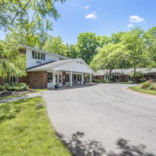 A beautiful residential house with a driveway surrounded by lush trees on a sunny day.