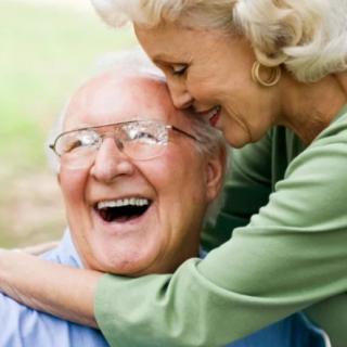 An elderly couple shares a joyful hug outdoors.