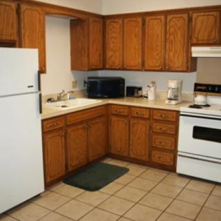 A spacious kitchen with wooden cabinets, featuring a refrigerator, stove, and microwave on a tile floor.