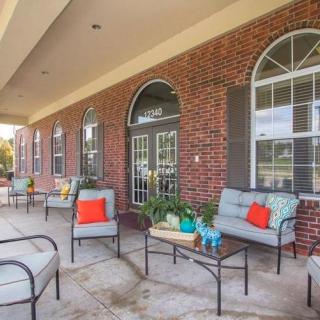 A cozy outdoor patio with cushioned seating and decorative plants against a brick wall.