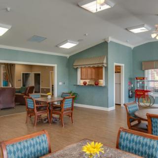 A cozy lounge area with tables and chairs, featuring blue walls and an adjoining kitchen space.