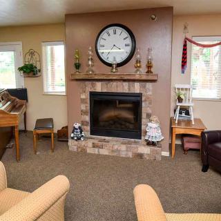 A cozy living room featuring a central fireplace with a large clock above it, surrounded by comfortable seating and home decor accents.