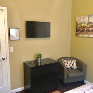 A cozy bedroom corner with a mounted TV, chest of drawers, and armchair.