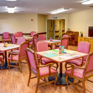 A spacious and well-lit dining room with several tables and chairs arranged neatly for communal use.