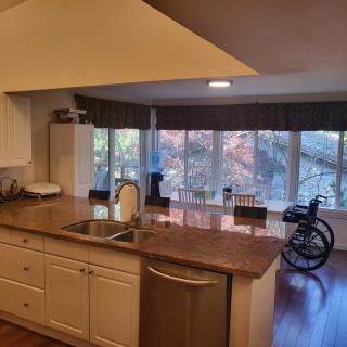 A spacious kitchen with a dining area featuring large windows and a wheelchair near the table.