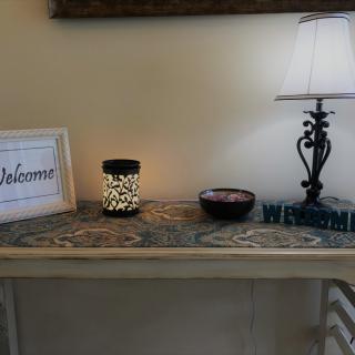 A cozy entryway table with a lamp, welcome sign, and decorative candle.