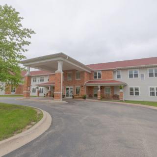 A two-story residential building with a covered entrance and driveway, surrounded by trees and a cloudy sky.