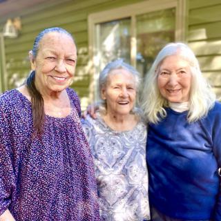 Three women smiling together outdoors, enjoying their time.
