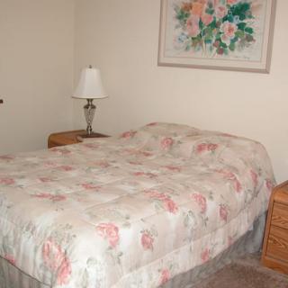 A cozy bedroom featuring a bed with a floral-patterned blanket, two wooden nightstands, and a flower painting above the bed.