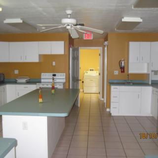 Spacious kitchen with white cabinets and a central island, featuring a ceiling fan and tiled flooring.