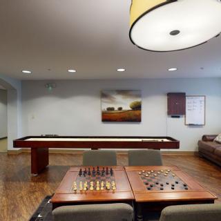 A cozy game room featuring a shuffleboard table, chess and checkers setup, comfortable seating, and stylish decor.