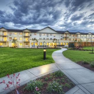 A scenic view of a residential building with a well-maintained lawn and walkway under a dramatic cloudy sky.