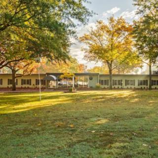 A scenic view of a building surrounded by trees with autumn foliage and a well-maintained lawn basking in sunlight.