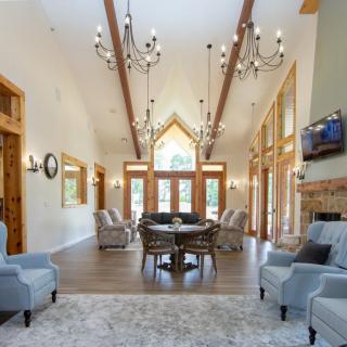 A spacious living room with vaulted ceilings, elegant chandeliers, and abundant natural light through large windows.