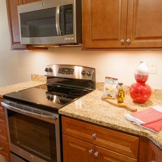 A modern kitchen with wooden cabinets, a stove, and a microwave over a granite countertop.