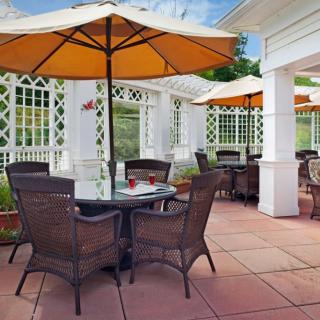 A sunny outdoor patio area with tables, wicker chairs, and large orange umbrellas.