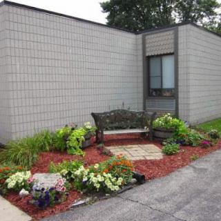 A peaceful garden area featuring a decorative bench surrounded by vibrant flowers and red mulch.