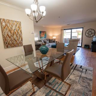 A modern open-plan dining and living room with a glass dining table, contemporary furniture, and decorative artwork.