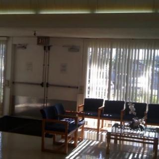 A bright waiting room with chairs and large windows covered by vertical blinds.