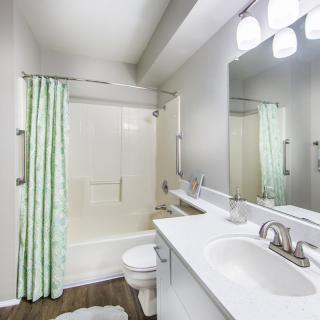 A modern bathroom with a shower, sink, and toilet, featuring bright lighting and a green shower curtain.