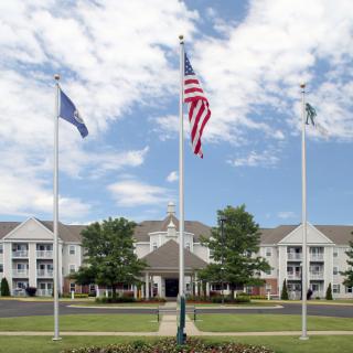 A building with three flagpoles and a landscaped foreground under a cloudy sky.