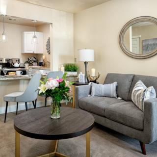 A modern living room with a cozy sofa, round coffee table, and decorative elements including flowers and a mirror.